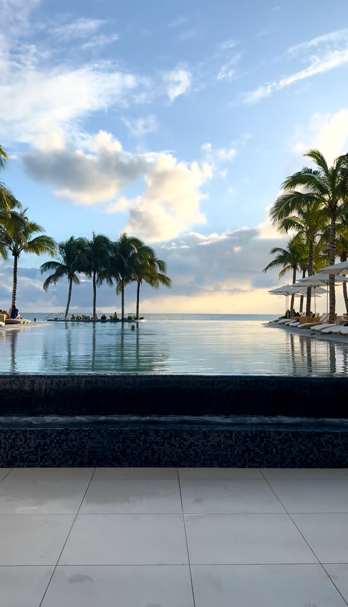 Palm trees cascading over a pool with clouds in the background