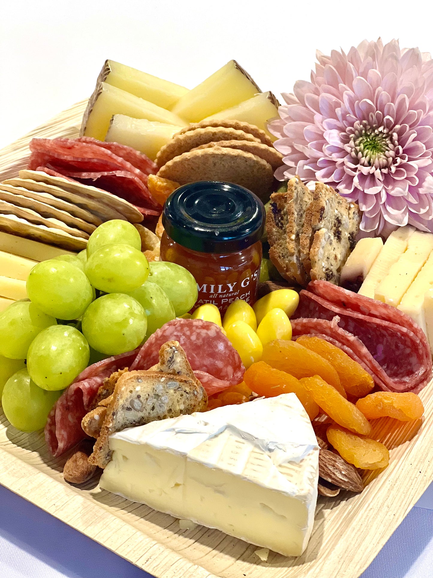 Charcuterie board with various cheeses, grapes, flowers, chocolate, crackers and cured meats