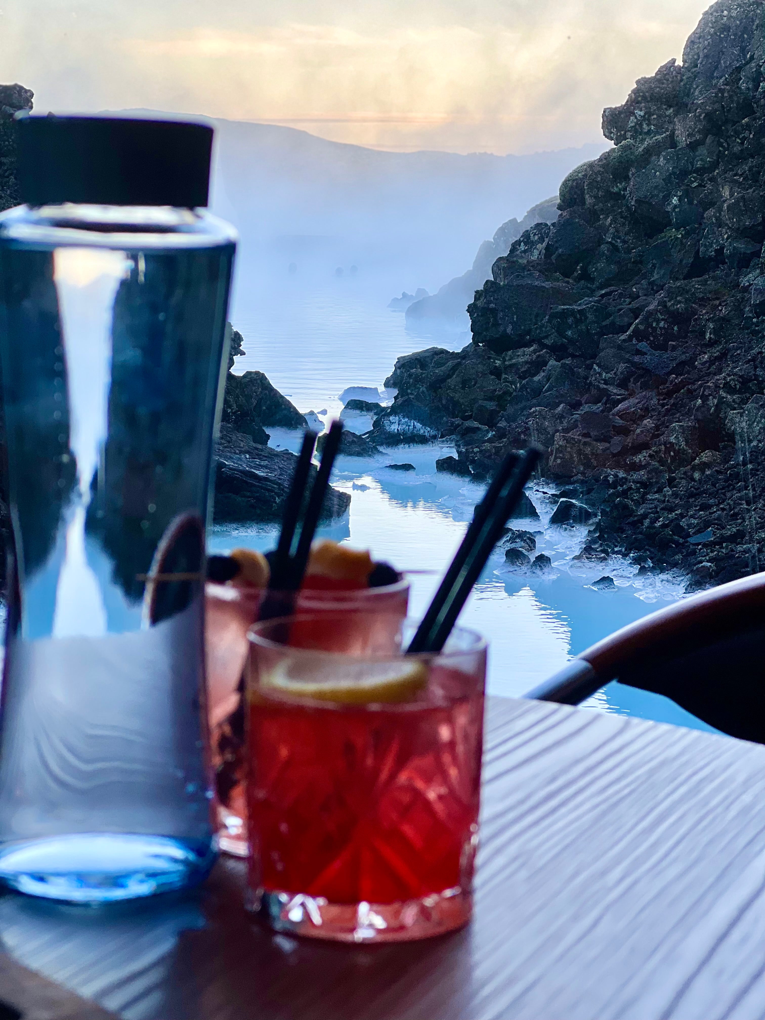 view of the blue lagoon from a restaurant with water and two cocktails on the table